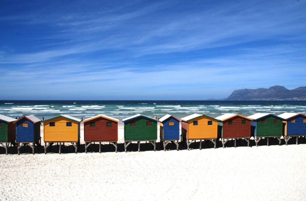 Colorful beach huts on a sunny seaside with scenic ocean views and mountains.