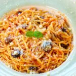 Close-up of a flavorful spaghetti dish topped with olives and parmesan cheese.